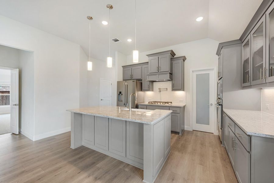 Kitchen with gray cabinets, large center island with granite countertop, and pendant lights overhead Kitchen with gray cabinets, large center island with granite countertop, and pendant lights overhead