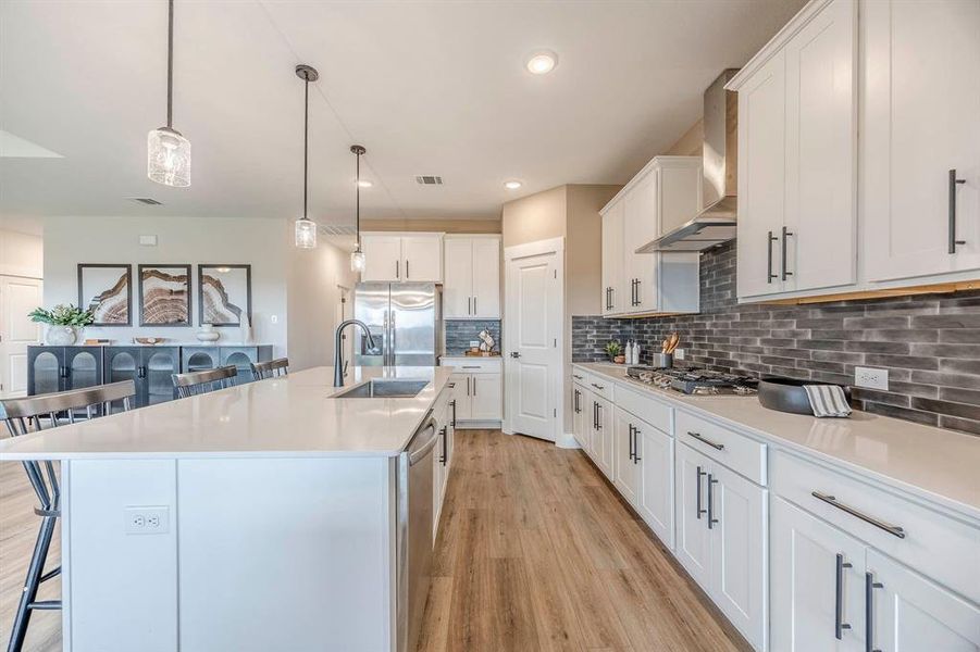 Kitchen with light wood-type flooring, wall chimney exhaust hood, an island with sink, white cabinetry, and stainless steel appliances