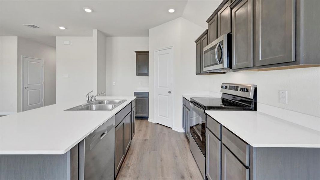 Kitchen featuring a double basin stainless steel sink, wood-finish flooring, recessed lighting, white countertops, and stainless steel appliances