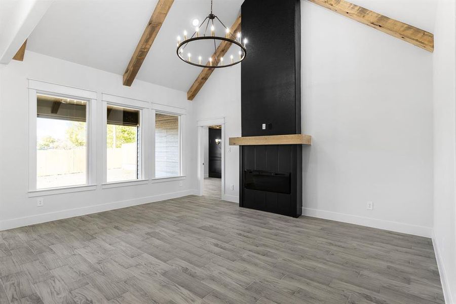 Unfurnished living room featuring hardwood / wood-style floors, beam ceiling, high vaulted ceiling, and an inviting chandelier