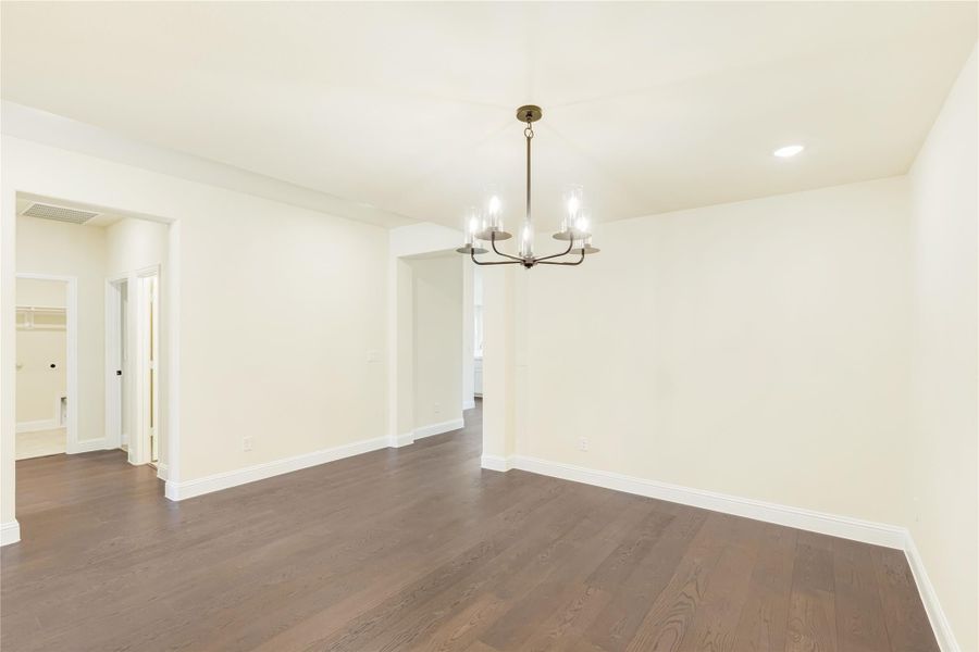 Empty dining room with dark hardwood floors, white walls, and a bronze chandelier overhead. Empty dining room with dark hardwood floors, white walls, and a bronze chandelier overhead.