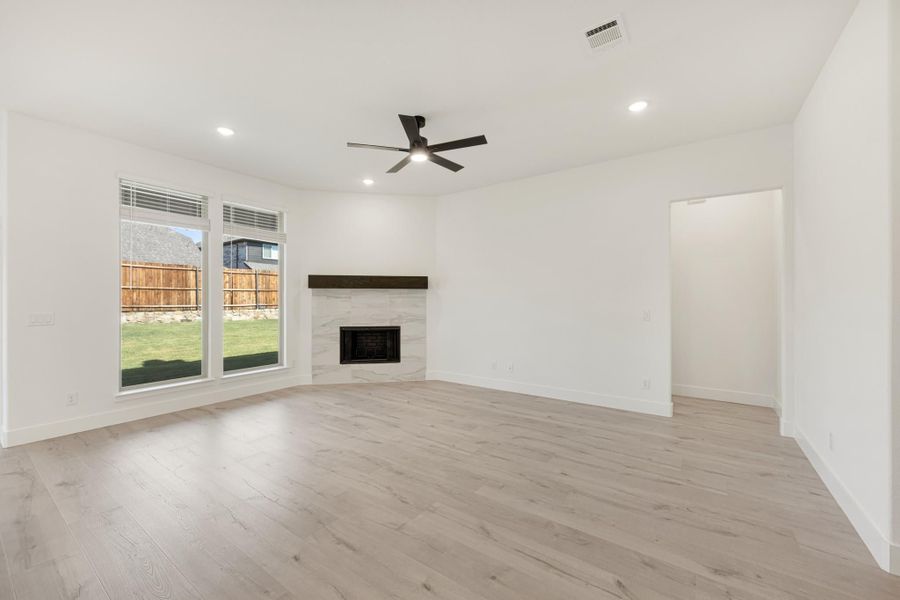 Open living room with light wood floors, tile fireplace, ceiling fan, and large windows