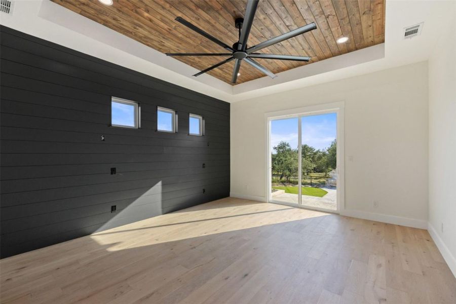 A spacious room features light wood flooring, a striking wood-paneled ceiling with a fan, and a glass sliding door opening to the outdoors. A spacious room features light wood flooring, a striking wood-paneled ceiling with a fan, and a glass sliding door opening to the outdoors.