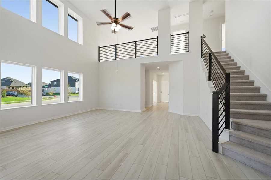 Two-story living area featuring high ceilings, light wood-finish flooring, a contemporary ceiling fan, and multiple large windows