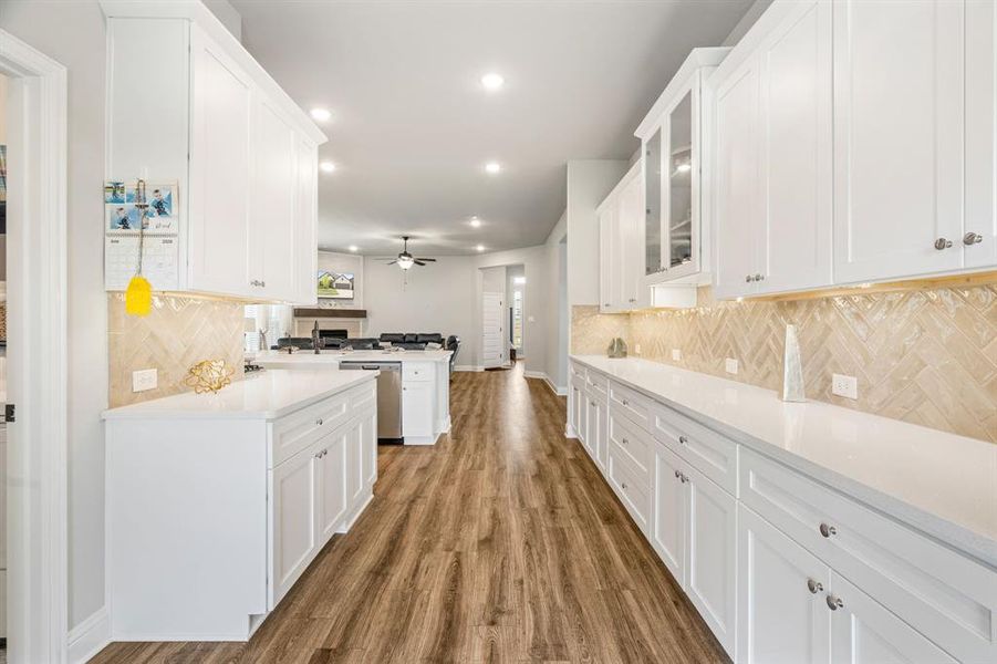 Galley kitchen featuring extensive white cabinetry, light-toned herringbone tile backsplash, white countertops, wood-finish flooring, and recessed lighting Galley kitchen featuring extensive white cabinetry, light-toned herringbone tile backsplash, white countertops, wood-finish flooring, and recessed lighting