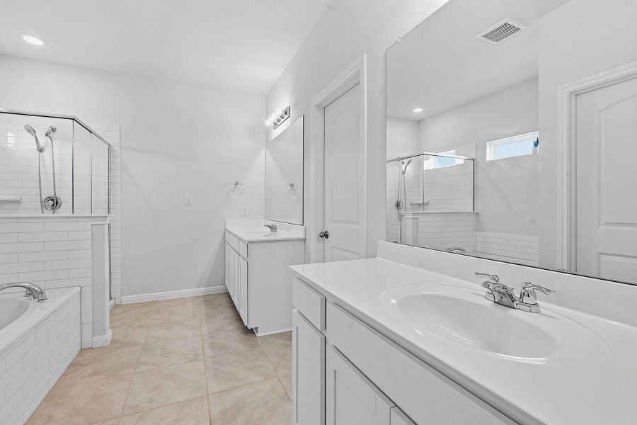 A well-lit primary bathroom features dual vanities, a separate tub, and a spacious glass-enclosed shower. A well-lit primary bathroom features dual vanities, a separate tub, and a spacious glass-enclosed shower.