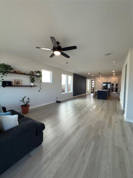 Expansive open-concept living area featuring light wood-finish flooring, a contemporary ceiling fan with integrated lighting, and multiple windows