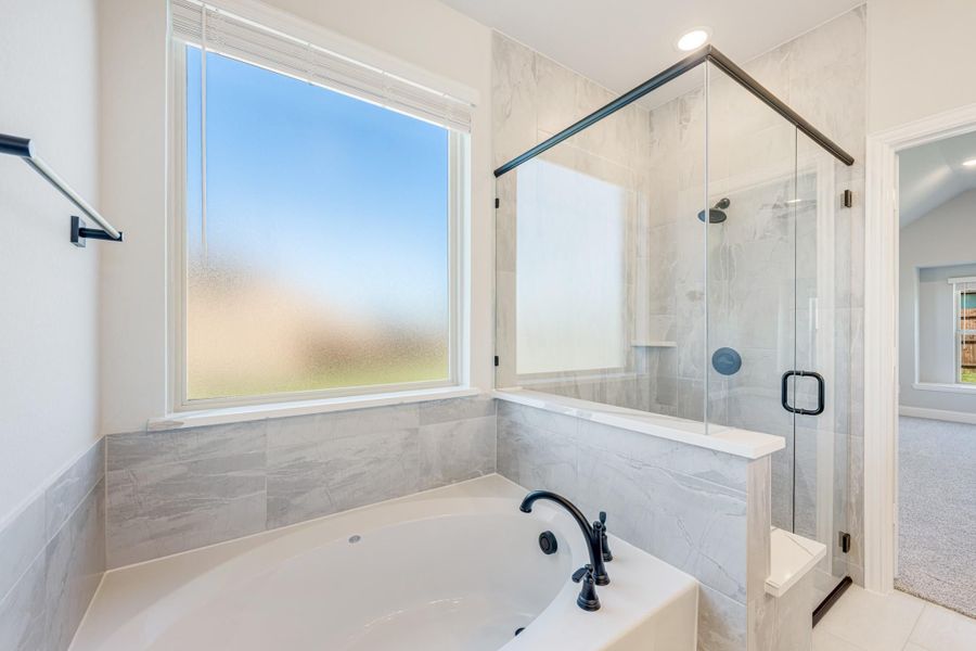 Bathroom with soaking tub, glass-enclosed shower, marble tile walls, and black fixtures Bathroom with soaking tub, glass-enclosed shower, marble tile walls, and black fixtures