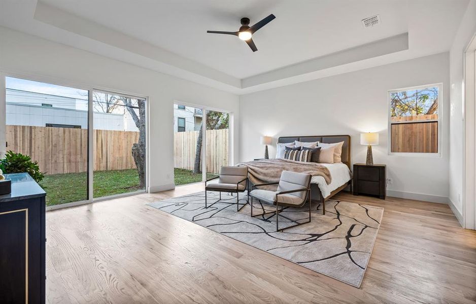 Bedroom featuring ceiling fan, access to outside, a tray ceiling, and light hardwood / wood-style flooring