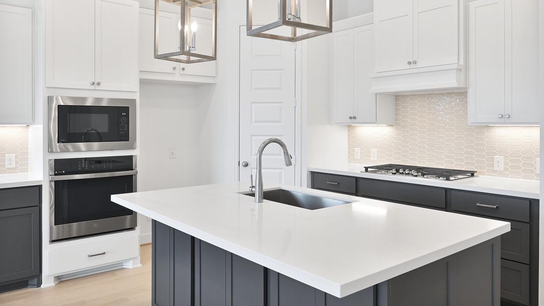 Kitchen featuring decorative backsplash, stainless steel appliances, white cabinets, gray cabinetry, and a center island with sink