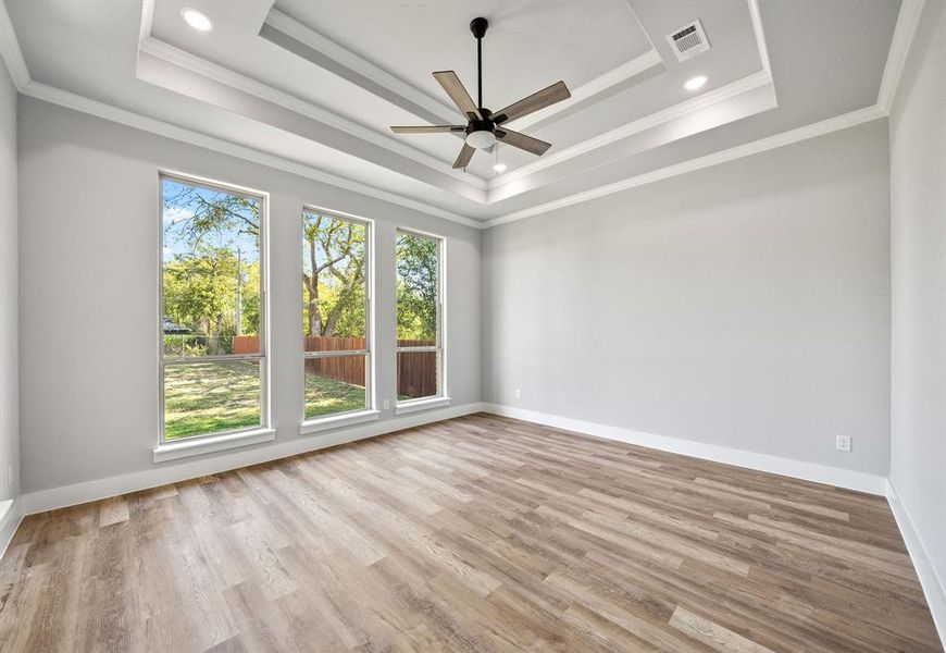 Spare room with crown molding, light wood-type flooring, a raised ceiling, and a ceiling fan