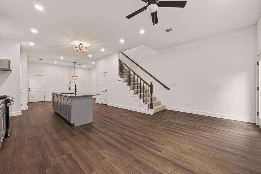 This spacious open-concept living area features sleek engineer wood floors, a modern kitchen island with a dark countertop, and a stylish ceiling fan. The area is well-lit with recessed lighting, and a staircase with wooden railings leads to the upper level, making it ideal for entertaining and comfortable living. This spacious open-concept living area features sleek engineer wood floors, a modern kitchen island with a dark countertop, and a stylish ceiling fan. The area is well-lit with recessed lighting, and a staircase with wooden railings leads to the upper level, making it ideal for entertaining and comfortable living.