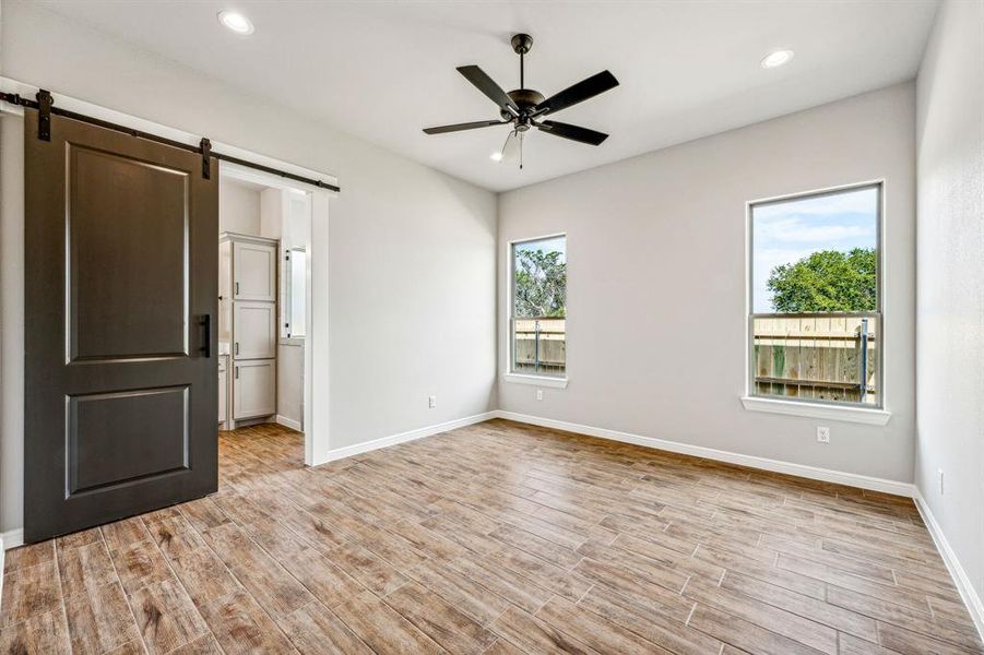 Empty room featuring light wood-type flooring, plenty of natural light, ceiling fan, and a barn door