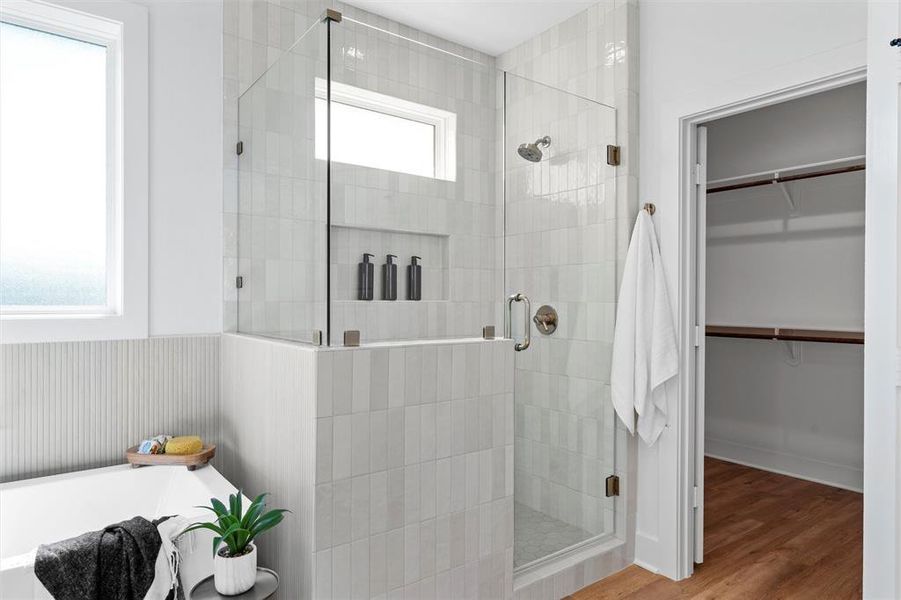 Bathroom featuring a walk in closet, a stall shower, a bath, and wood finished floors