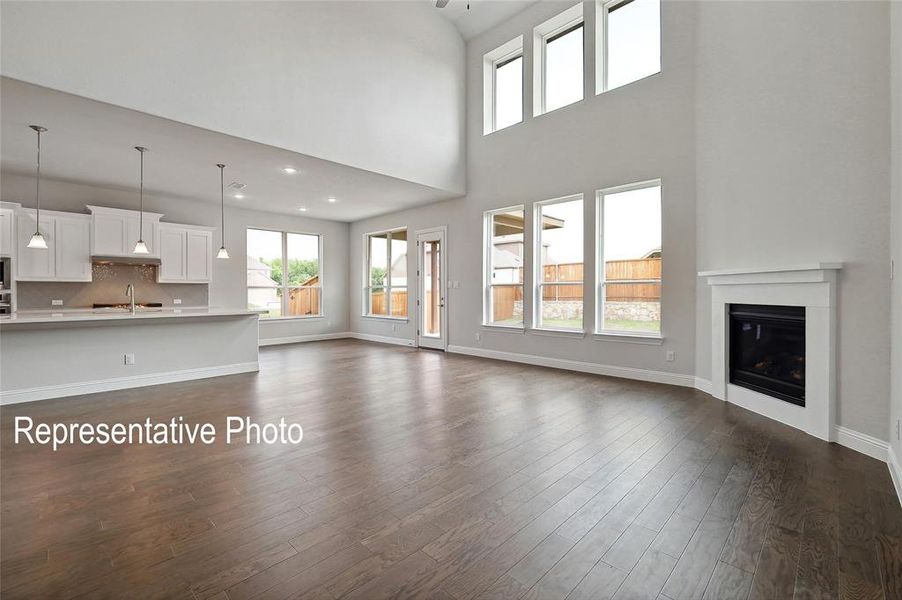 Spacious living area featuring wood-finish flooring, a fireplace with a white mantel, and high ceilings