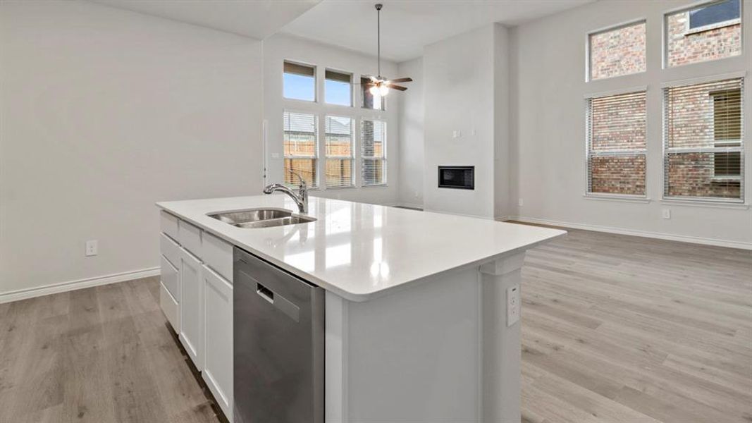 Kitchen with a glass covered fireplace, dishwasher, open floor plan, light wood-style flooring, and a center island with sink