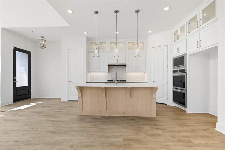 Kitchen featuring glass insert cabinets, a breakfast bar area, light wood finished floors, backsplash, and white cabinets Kitchen featuring glass insert cabinets, a breakfast bar area, light wood finished floors, backsplash, and white cabinets