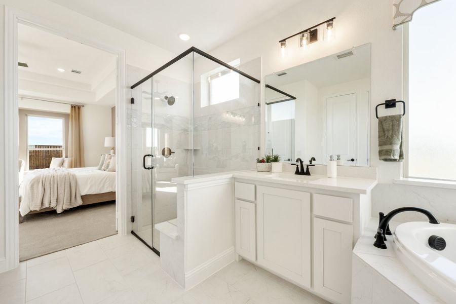 Master bathroom with glass walk-in shower, white vanity, soaking tub, and view into bedroom