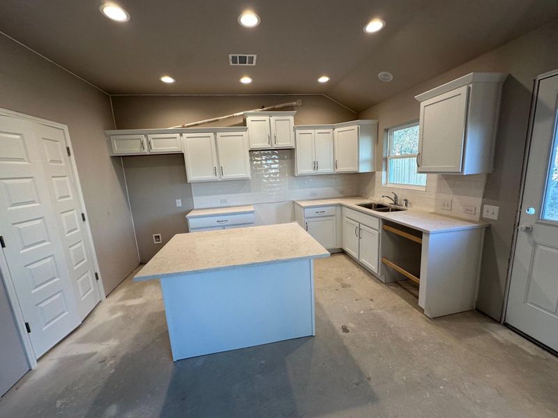 Kitchen featuring lofted ceiling, white cabinets, and a center island
