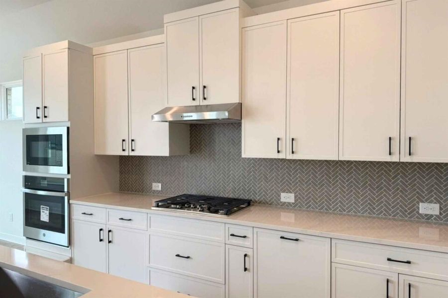 Kitchen featuring white cabinets, stainless steel appliances, decorative backsplash, and light stone counters