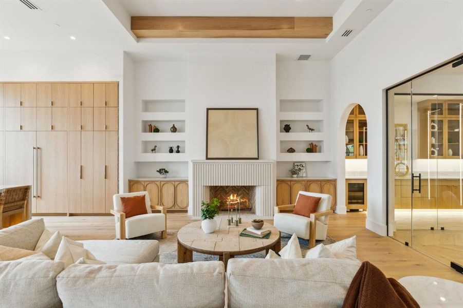 Living room with light wood finished floors, built in features, a cast stone fireplace, beverage cooler, wine cellar and arched walkways Living room with light wood finished floors, built in features, a cast stone fireplace, beverage cooler, wine cellar and arched walkways
