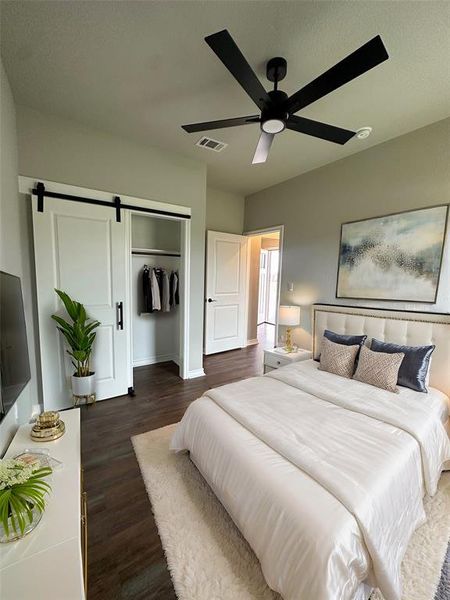 Bedroom with dark hardwood / wood-style flooring, a closet, a barn door, and ceiling fan