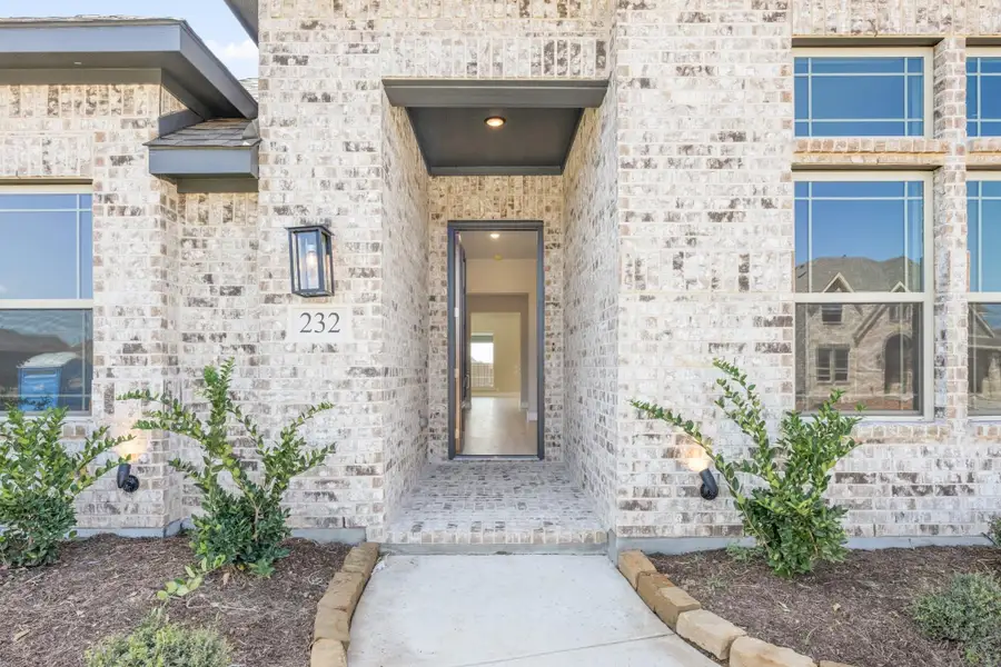 Front entry of brick home with open door, wall sconce, house number 232, and landscaped walkway