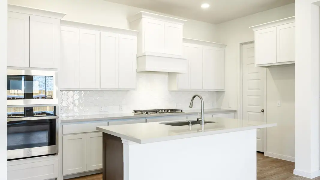 Kitchen with tasteful backsplash, appliances with stainless steel finishes, light countertops, an island with sink, and light wood-style floors Kitchen with tasteful backsplash, appliances with stainless steel finishes, light countertops, an island with sink, and light wood-style floors