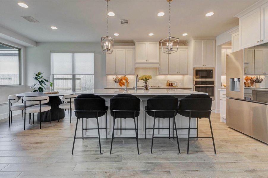 This modern kitchen features white cabinetry, stainless steel appliances, and a large island with seating for four. The space is bright and open, with pendant lighting and a cozy dining area by the window. This modern kitchen features white cabinetry, stainless steel appliances, and a large island with seating for four. The space is bright and open, with pendant lighting and a cozy dining area by the window.