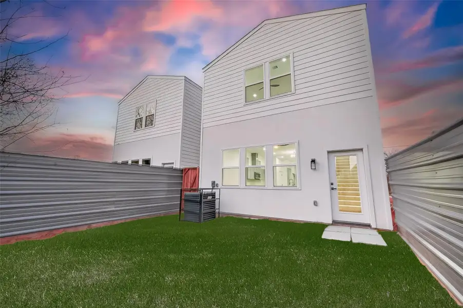 Modern two-story home with a clean white exterior, fenced yard, and outdoor lighting. Features large windows for ample natural light, complemented by a well-maintained lawn and a beautiful sunset backdrop.