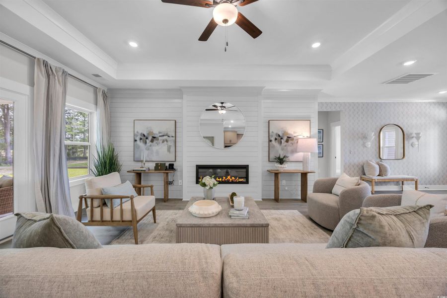 Living area with a tray ceiling, a large fireplace, wood finished floors, a ceiling fan, and recessed lighting