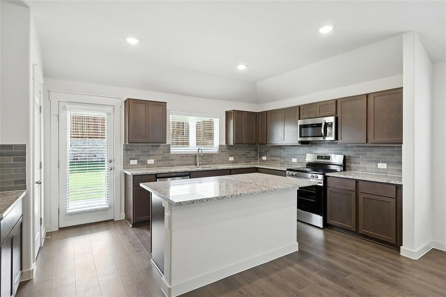 Kitchen with stainless steel appliances, decorative backsplash, dark wood finished floors, a kitchen island, and recessed lighting Kitchen with stainless steel appliances, decorative backsplash, dark wood finished floors, a kitchen island, and recessed lighting