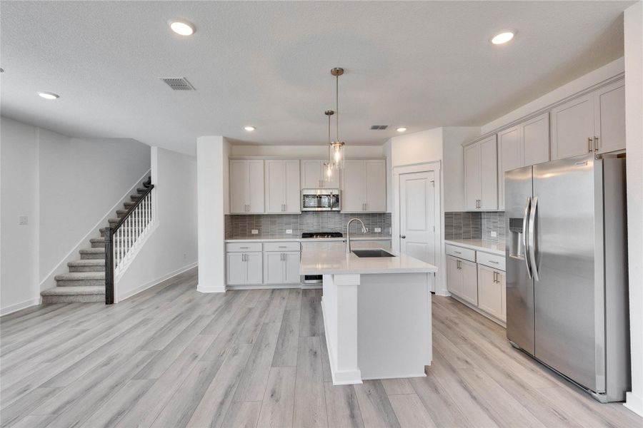 Kitchen with stainless steel appliances, pendant lighting, light wood-style floors, backsplash, and an island with sink Kitchen with stainless steel appliances, pendant lighting, light wood-style floors, backsplash, and an island with sink