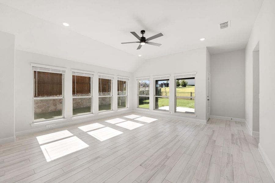 Bright empty living room with vaulted ceiling, ceiling fan, light wood floors, and large windows overlooking backyard
