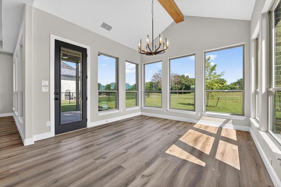 Vaulted ceiling with an exposed wood beam, modern chandelier, wood-finish flooring, and multiple picture windows
