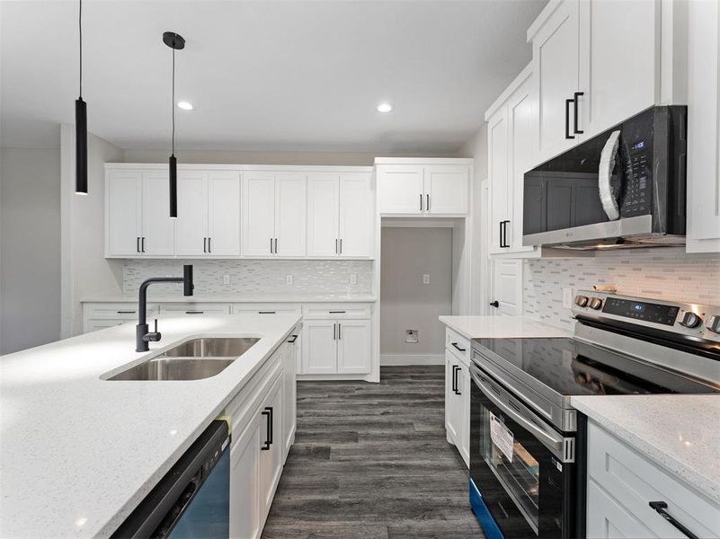 Kitchen with light stone counters, stainless steel appliances, sink, white cabinetry, and hanging light fixtures