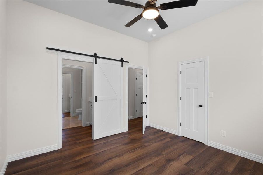 Unfurnished bedroom featuring baseboards, a barn door, ceiling fan, recessed lighting, and dark wood-type flooring