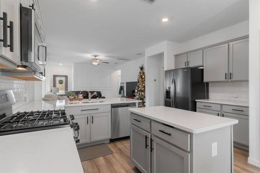 Kitchen with appliances with stainless steel finishes, gray cabinetry, ceiling fan, sink, and a kitchen island