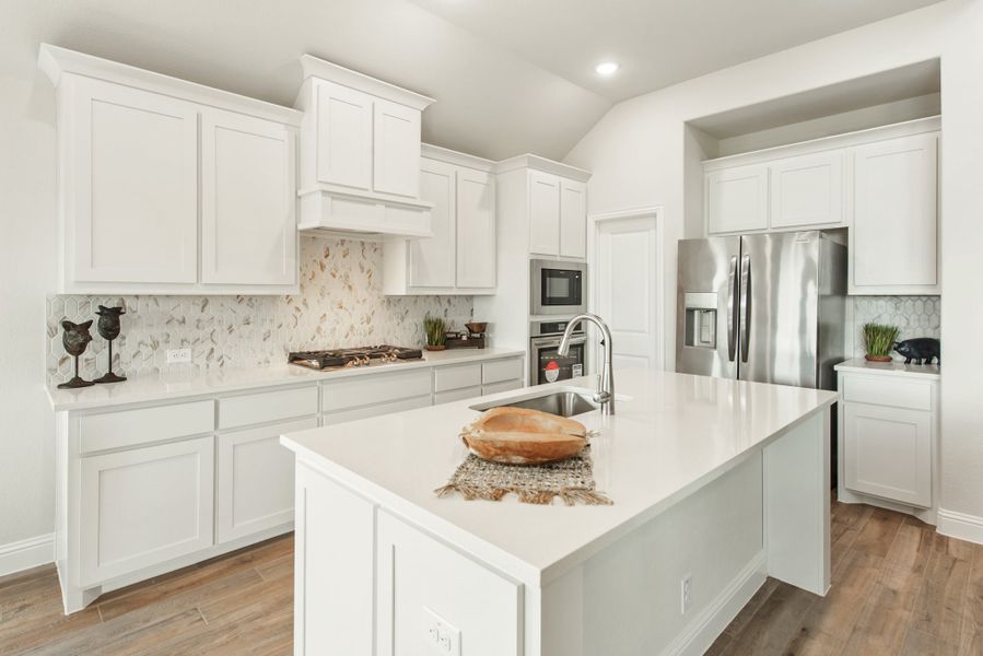 Kitchen with white cabinets, center island with sink, stainless steel appliances, and decorative tile backsplash on hardwood floors