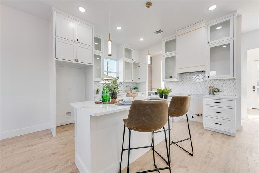 Kitchen with light wood-type flooring, backsplash, decorative light fixtures, white cabinets, and a center island