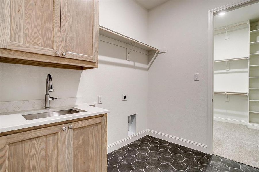 Utility room featuring electric dryer hookup, sink, tile floors, and custom cabinets