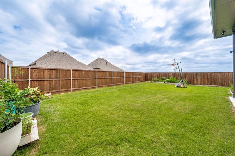 Expansive backyard featuring a lush lawn, privacy fencing, and a concrete patio section