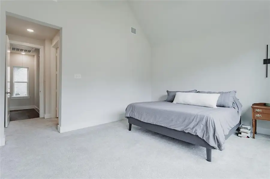 Vaulted ceiling bedroom featuring light-colored carpeting, recessed lighting, and a hallway entry