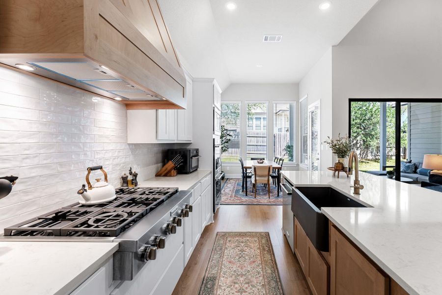 Gourmet kitchen featuring a professional-grade range, wood-finish hood, white tile backsplash, light-toned countertops, and a dark-toned apron front sink