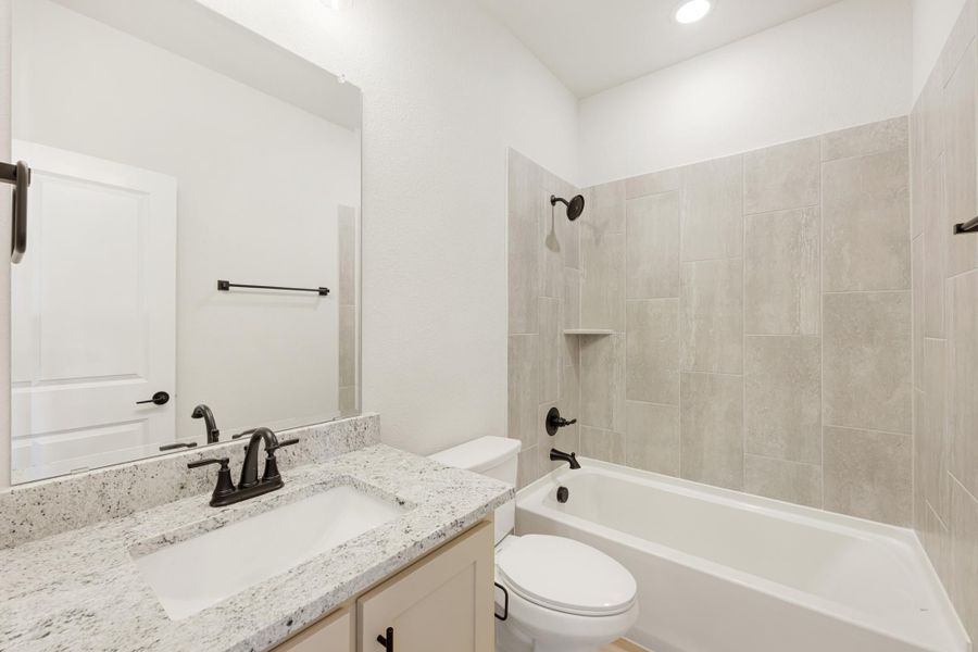 Bathroom with granite vanity, white tub-shower combo with gray tile surround, and dark bronze fixtures