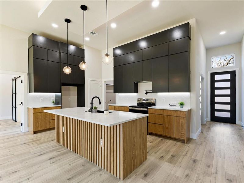 Kitchen with modern cabinets, hanging light fixtures, dark cabinets, light wood finished floors, and an island with sink