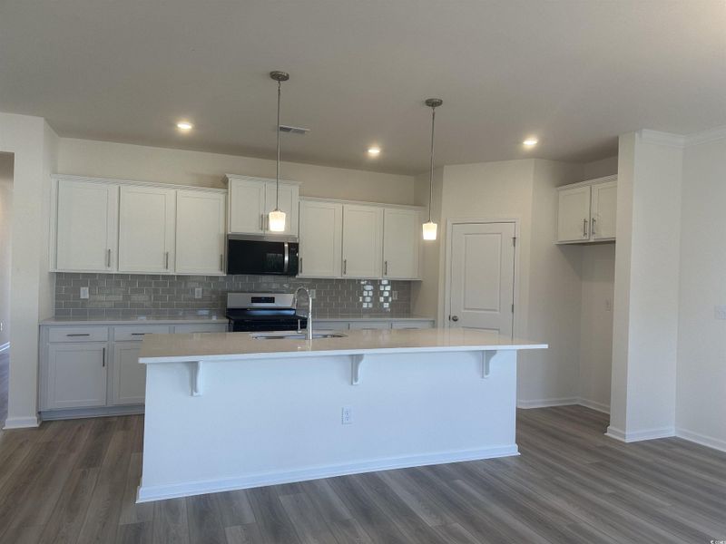 Kitchen featuring backsplash, white cabinets, decorative light fixtures, stainless steel appliances, and a center island with sink