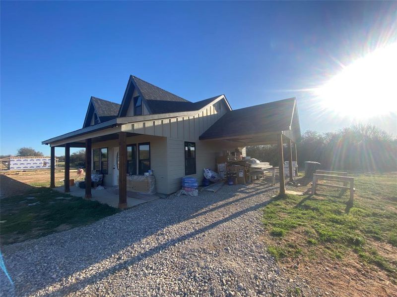 View of home's exterior with board and batten siding, a patio area, an attached carport, gravel driveway, and a lawn