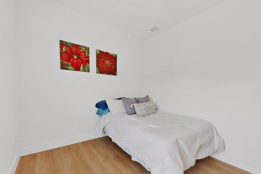 Room featuring wood-finish flooring, white baseboards, and neutral wall tones Room featuring wood-finish flooring, white baseboards, and neutral wall tones