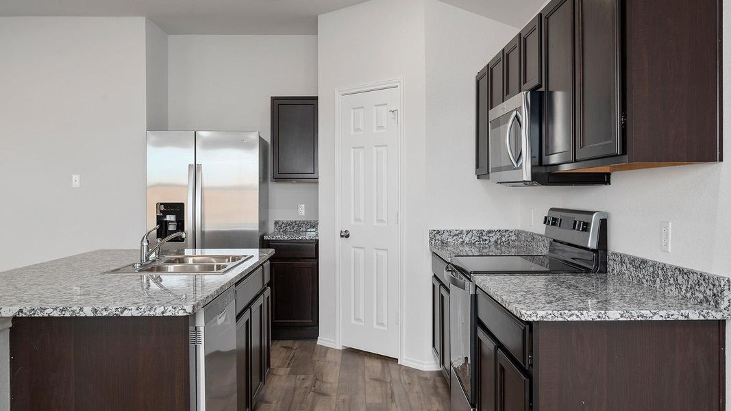 Kitchen with appliances with stainless steel finishes, a kitchen island with sink, dark brown cabinetry, and light stone countertops